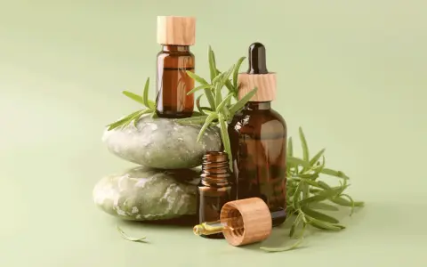 Flaconi ambrati con gocce e rametti di rosmarino, che evocano le proprietà dell'olio essenziale di rosmarino.