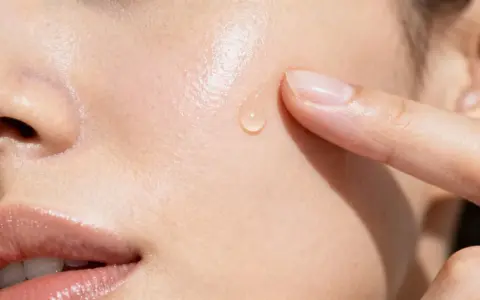 Goccia di siero sulla pelle, un tocco delicato. La niacinamide a cosa serve? Migliora la barriera cutanea e riduce le imperfezioni.