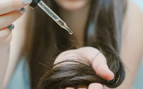 Goccia di olio di ricino su capelli scuri. Scopri a cosa serve l'olio di ricino per la cura dei capelli e della pelle.