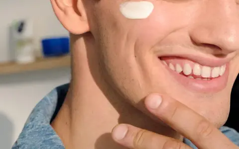 Uomo sorridente applica crema sul viso, forse per lenire l'irritazione da lametta quanto dura.