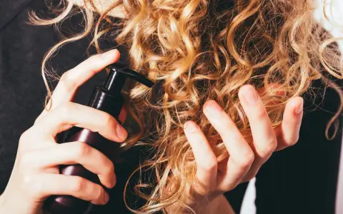 Mani che applicano un prodotto su capelli ricci secchi, per nutrirli e renderli morbidi.