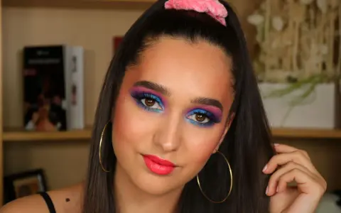 Ragazza con trucco occhi vivace blu e viola, labbra fucsia e scrunchie rosa. Un look ispirato al tutorial trucco anni 80.