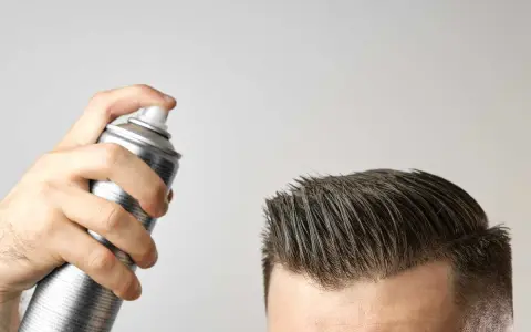 Mano che spruzza lacca sui capelli. Attenzione, la cera fa cadere i capelli, ma questo prodotto è per fissare.