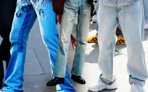 Gambe in primo piano con diversi modelli di moschino jeans: uno blu con inserti e ricami, uno più chiaro e sbiadito, e uno grigio chiaro oversize.