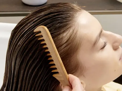 Una mano pettina delicatamente i capelli bagnati, sciogliendo eventuali nodi ai capelli dietro la nuca per una chioma fluente.