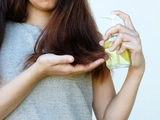 Donna applica olio di jojoba sui capelli, sfruttando le sue proprietà nutrienti per una chioma sana e lucente.
