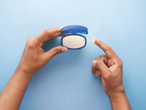 Mano che preleva vaselina per lenire l'irritazione da retinolo.