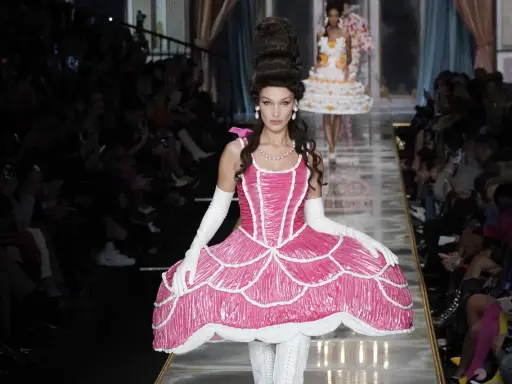 Modella con abito rosa Moschino abbigliamento donna, ispirato a una torta, con acconciatura voluminosa e guanti bianchi.