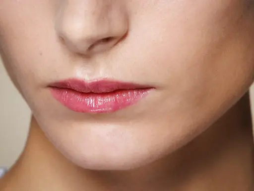 Labbra sottili valorizzate da un lucidalabbra rosa brillante, un trucco che dona volume e un aspetto pieno.