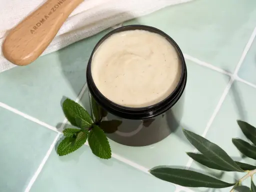 Vaso di scrub cuoio capelluto fai da te con menta e foglie d'ulivo. Un pettine in legno è visibile in alto a sinistra.