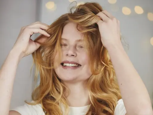 Ragazza con capelli rossi mossi che si sistema la chioma, un gesto per dare volume ai capelli.