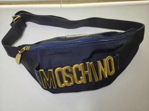 Borsa blu Moschino con logo dorato in rilievo, tracolla regolabile e zip. Un accessorio iconico per un look audace.