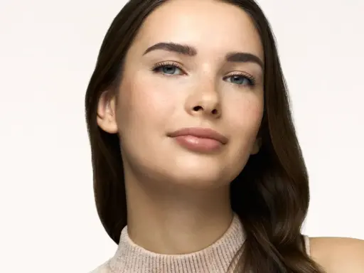 Primo piano di una giovane donna con lentiggini, labbra lucide e sopracciglia definite. Un look naturale, perfetto come trucco da fare per ogni occasione.