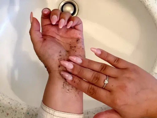 Mani con scrub per capire come togliere l'autoabbronzante. Unghie rosa e anello con cuore.