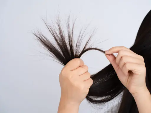 Mani che esaminano ciocche di capelli scuri, mostrando le doppie punte come causa di capelli danneggiati e secchi.