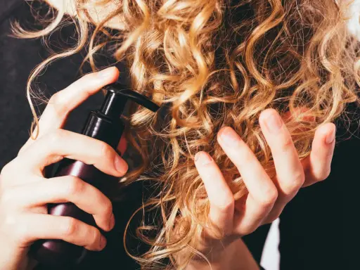 Mani che applicano un prodotto su capelli ricci secchi, per nutrirli e renderli morbidi.