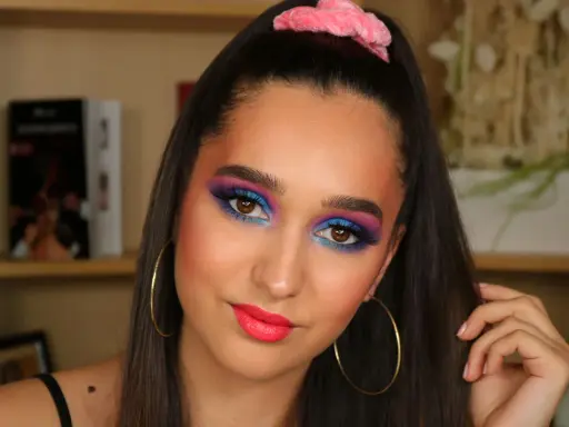 Ragazza con trucco occhi vivace blu e viola, labbra fucsia e scrunchie rosa. Un look ispirato al tutorial trucco anni 80.