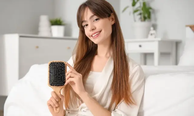 Ragazza sorridente mostra una spazzola per capelli in plastica, perfetta per districare e pulire i capelli.