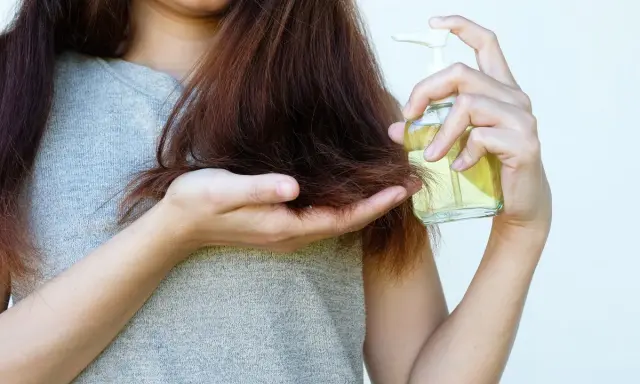 Donna applica olio di jojoba sui capelli, sfruttando le sue proprietà nutrienti per una chioma sana e lucente.