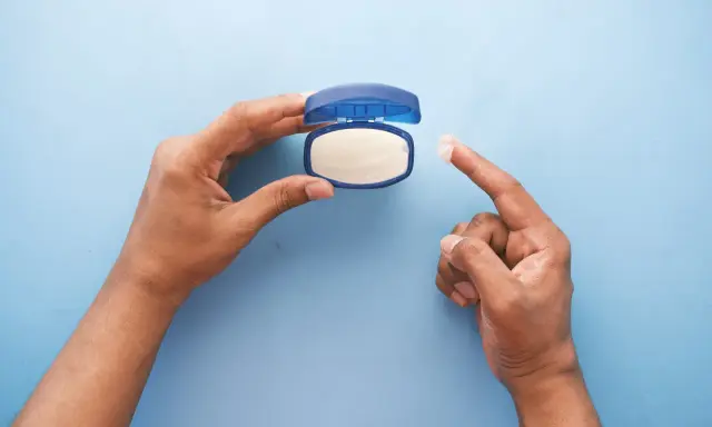 Mano che preleva vaselina per lenire l'irritazione da retinolo.
