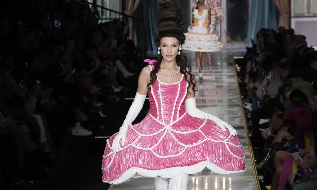 Modella con abito rosa Moschino abbigliamento donna, ispirato a una torta, con acconciatura voluminosa e guanti bianchi.