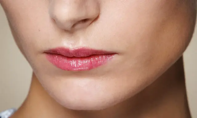 Labbra sottili valorizzate da un lucidalabbra rosa brillante, un trucco che dona volume e un aspetto pieno.