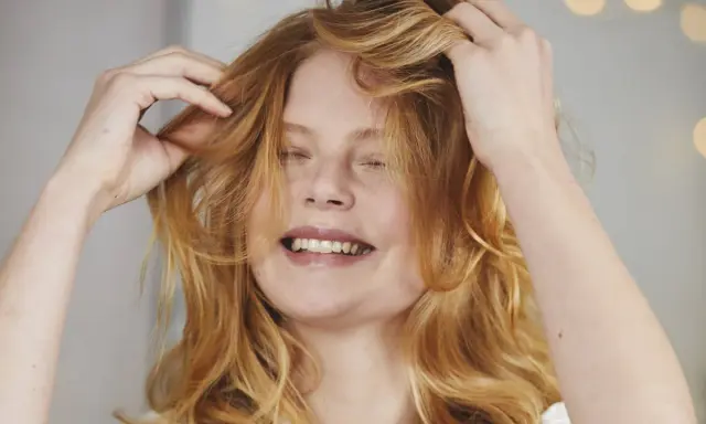 Ragazza con capelli rossi mossi che si sistema la chioma, un gesto per dare volume ai capelli.
