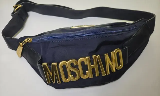 Borsa blu Moschino con logo dorato in rilievo, tracolla regolabile e zip. Un accessorio iconico per un look audace.