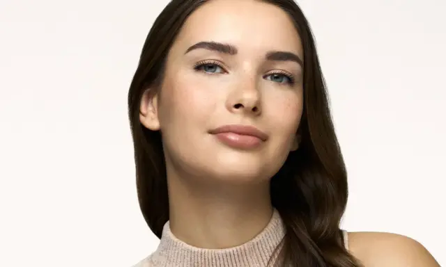 Primo piano di una giovane donna con lentiggini, labbra lucide e sopracciglia definite. Un look naturale, perfetto come trucco da fare per ogni occasione.