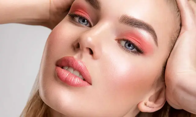 Viso di donna con trucco pesca: ombretto vivace, labbra lucide e un tocco di fard dove si mette il fard per un effetto radioso.