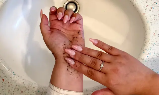 Mani con scrub per capire come togliere l'autoabbronzante. Unghie rosa e anello con cuore.