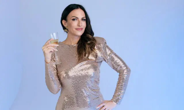 Donna con un abito pavone scintillante, tiene un bicchiere di champagne, pronta per festeggiare.