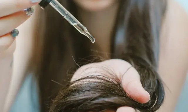 Goccia di olio di ricino su capelli scuri. Scopri a cosa serve l'olio di ricino per la cura dei capelli e della pelle.