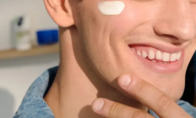 Uomo sorridente applica crema sul viso, forse per lenire l'irritazione da lametta quanto dura.