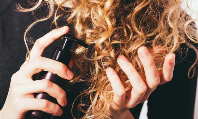 Mani che applicano un prodotto su capelli ricci secchi, per nutrirli e renderli morbidi.