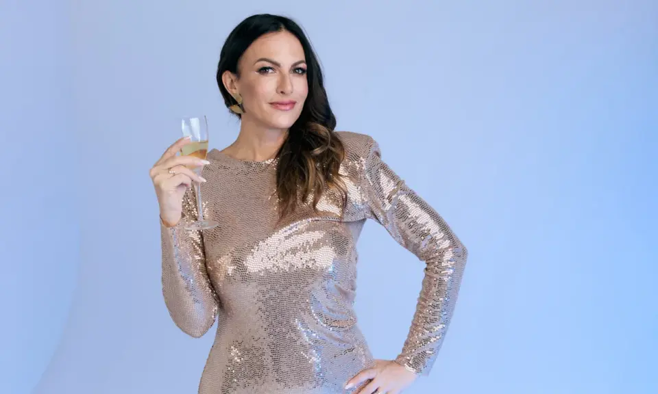Donna con un abito pavone scintillante, tiene un bicchiere di champagne, pronta per festeggiare.