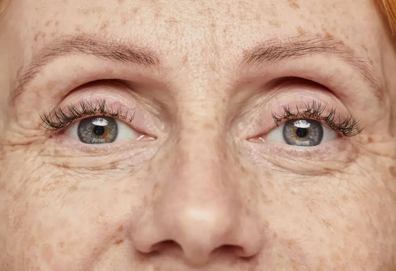 Occhi di donna con lentiggini e ciglia lunghe. Un esempio di come truccarsi a 50 anni per valorizzare la bellezza naturale.