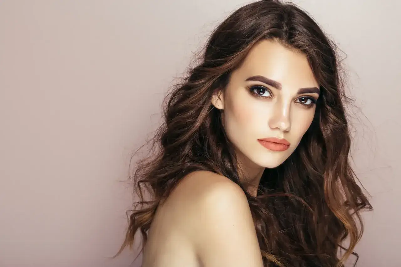 Modella con capelli castani mossi e un trucco per more che esalta gli occhi e le labbra con un tocco di colore naturale.