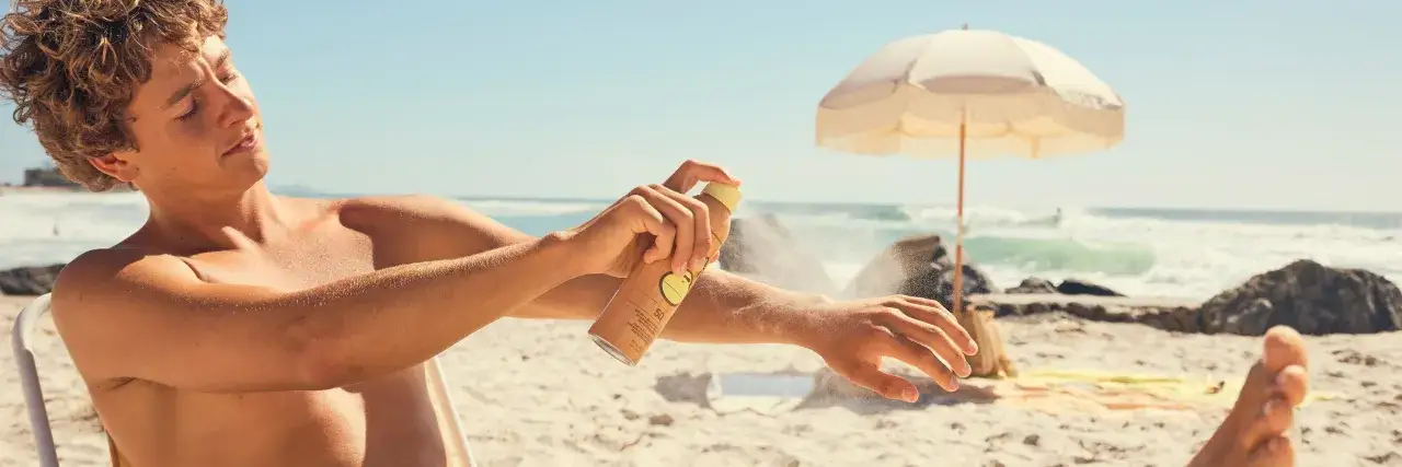 Ragazzo sulla spiaggia applica spray solare con protezione 50 che dura 50 minuti.