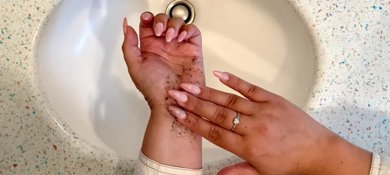 Mani con scrub per capire come togliere l'autoabbronzante. Unghie rosa e anello con cuore.