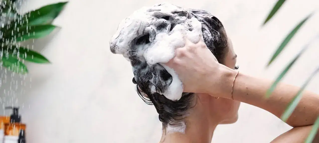 Donna lava i capelli con abbondante schiuma, un gesto che risponde alla domanda: ogni quanto lavare i capelli grassi per mantenerli puliti e freschi.