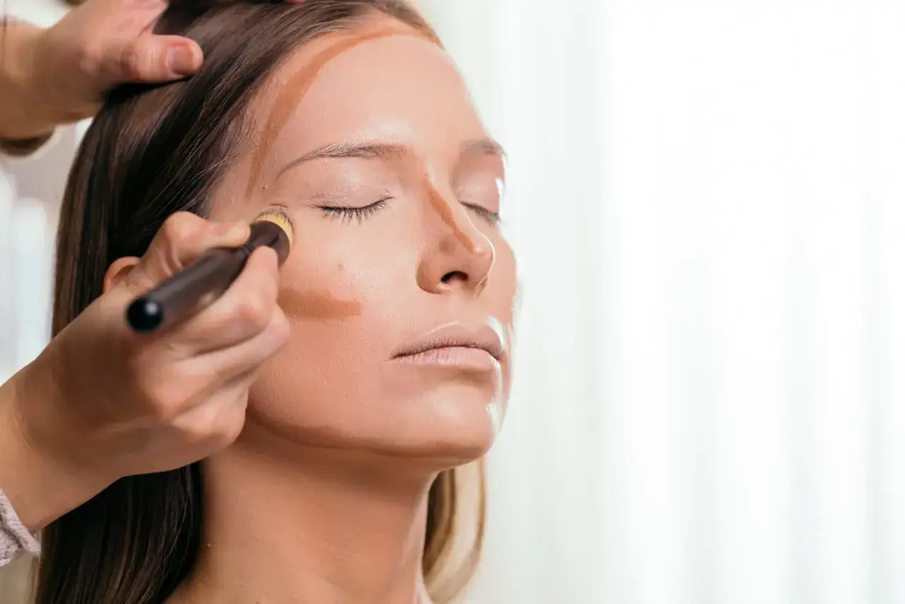 Applicazione di makeup contouring con pennello su zigomi, fronte e naso per scolpire il viso.