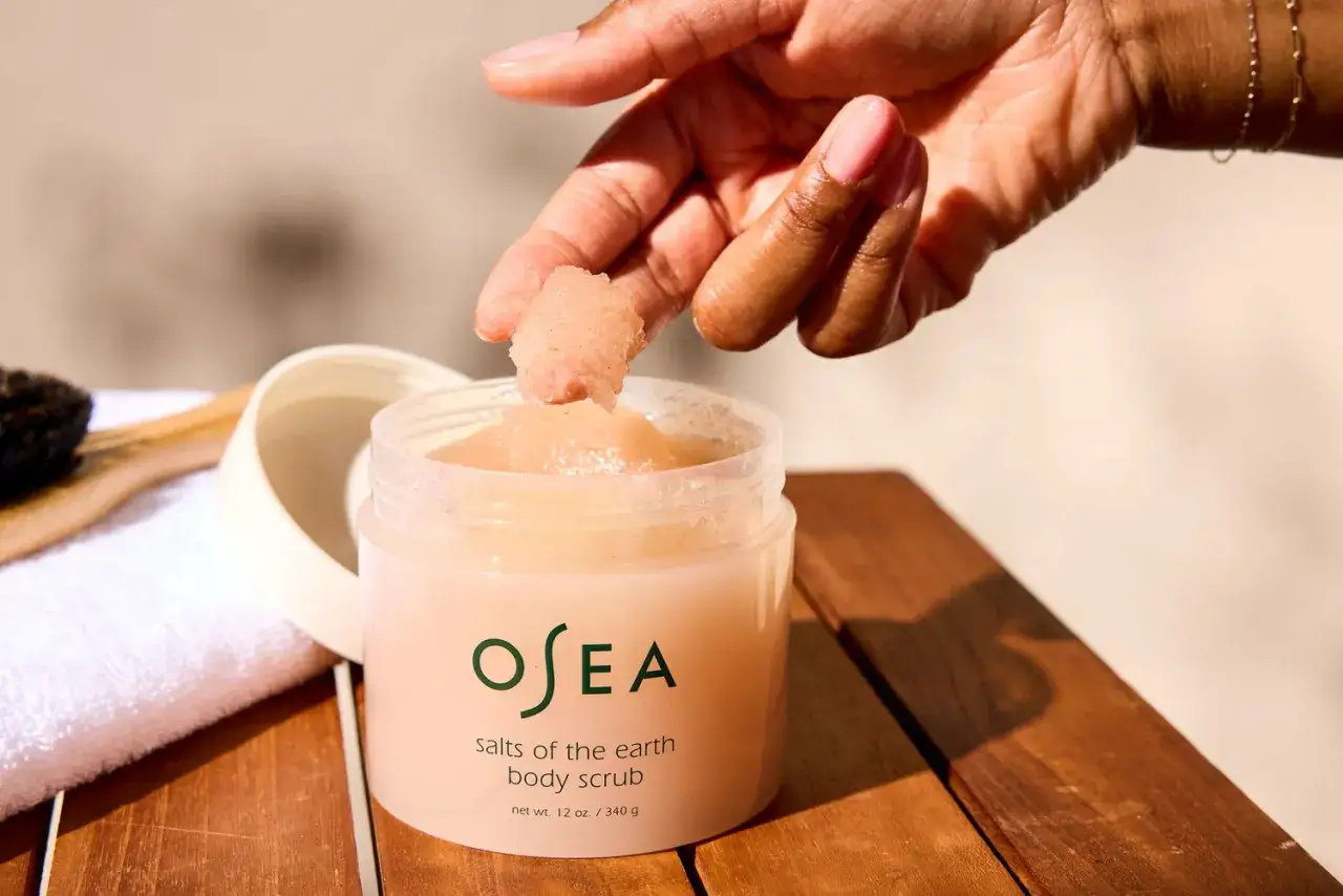 Mano che preleva scrub corpo OSEA per rimuovere la pelle morta. Un rituale di bellezza per una pelle liscia.