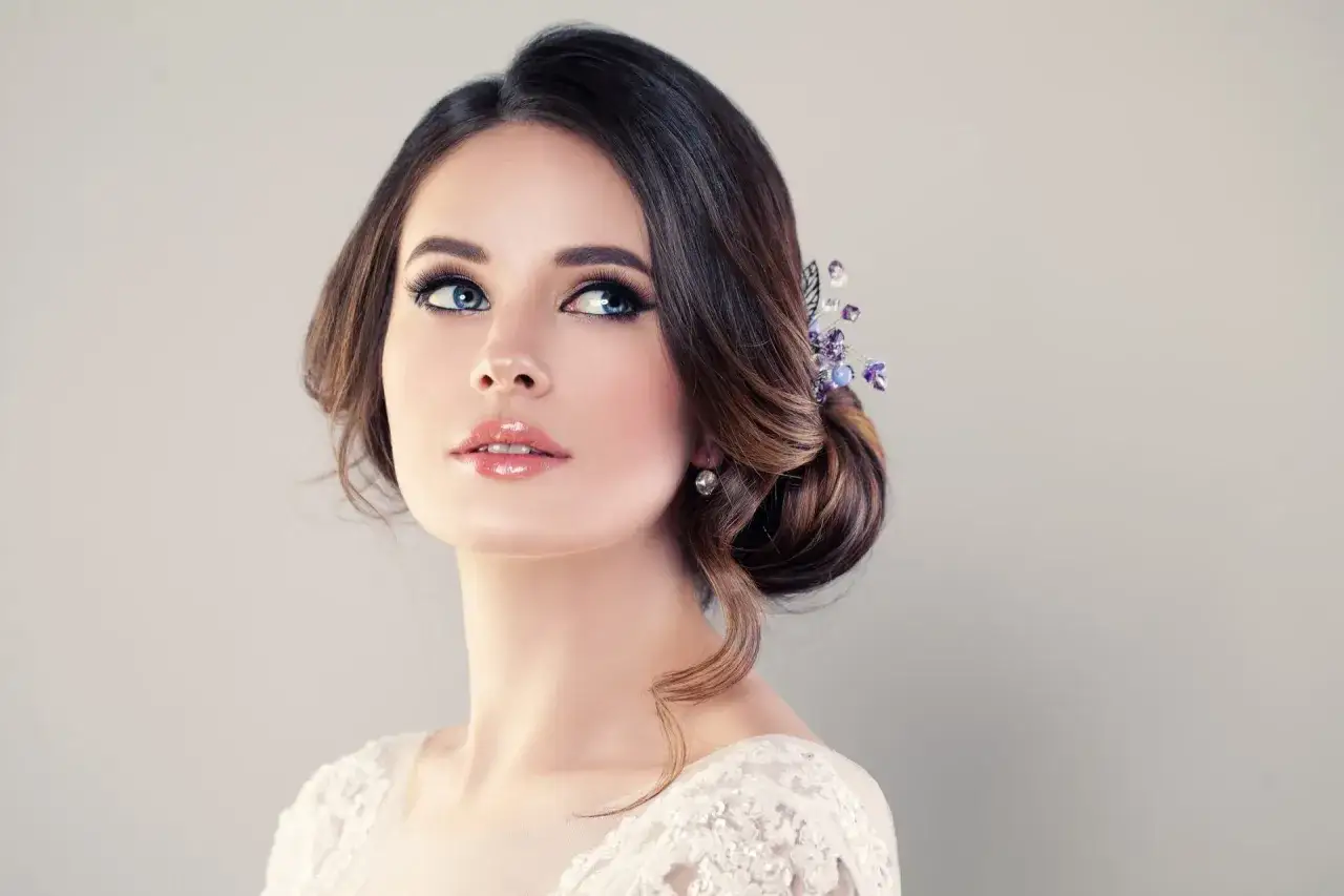 Donna con acconciatura raccolta e un make up elegante, impreziosita da un fermaglio con cristalli viola e orecchini luminosi.