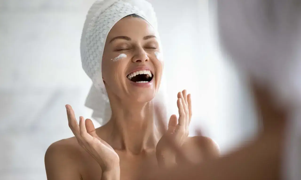 Donna con turbante e crema sul viso, felice durante la sua night skincare routine.