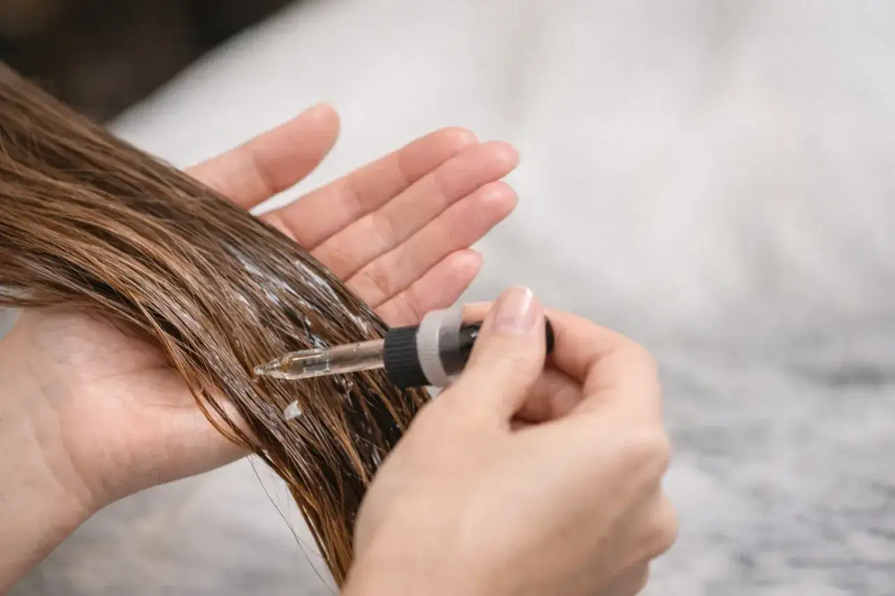 Mani applicano un balsamo nutriente sui capelli umidi con un contagocce, per lasciarlo agire tutta la notte e ottenere una chioma setosa.