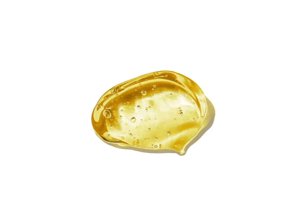 Goccia dorata di gel con bollicine, un esempio di ammonium acryloyldimethyltaurate/vp copolymer, su sfondo bianco.
