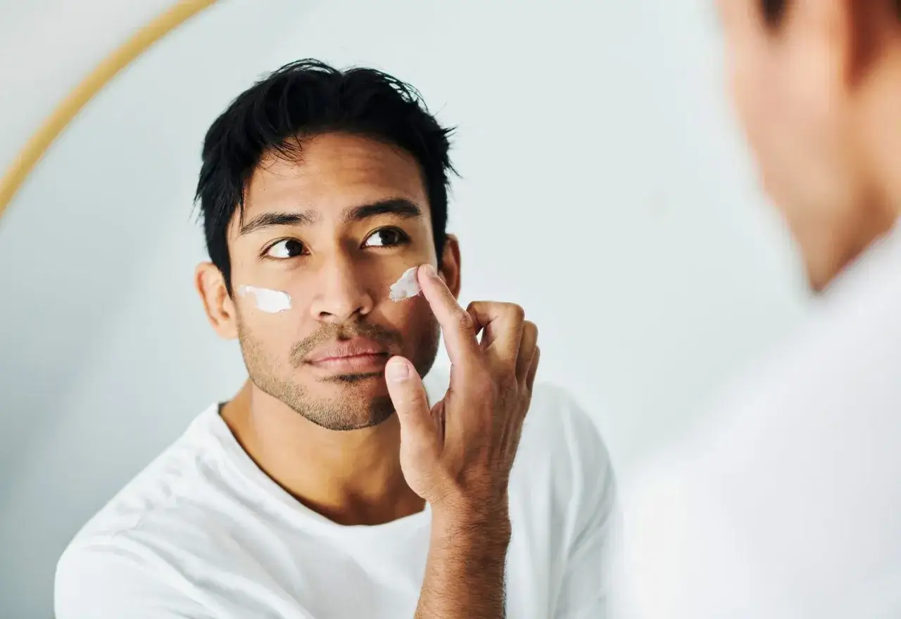 Uomo si applica crema sul viso, usando la crema solare come crema idratante per proteggere la pelle.