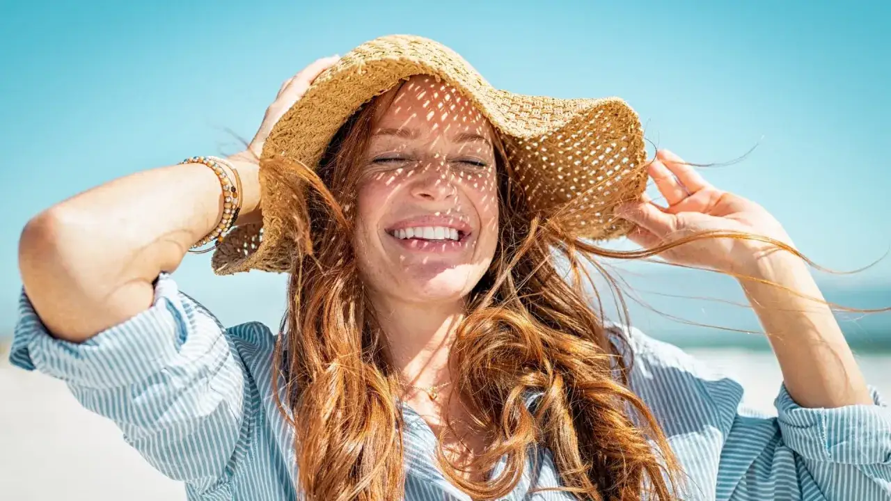 Donna sorridente con cappello di paglia, la luce del sole crea ombre sul viso. La sua pelle, forse trattata con acido salicilico, appare luminosa sotto il sole.