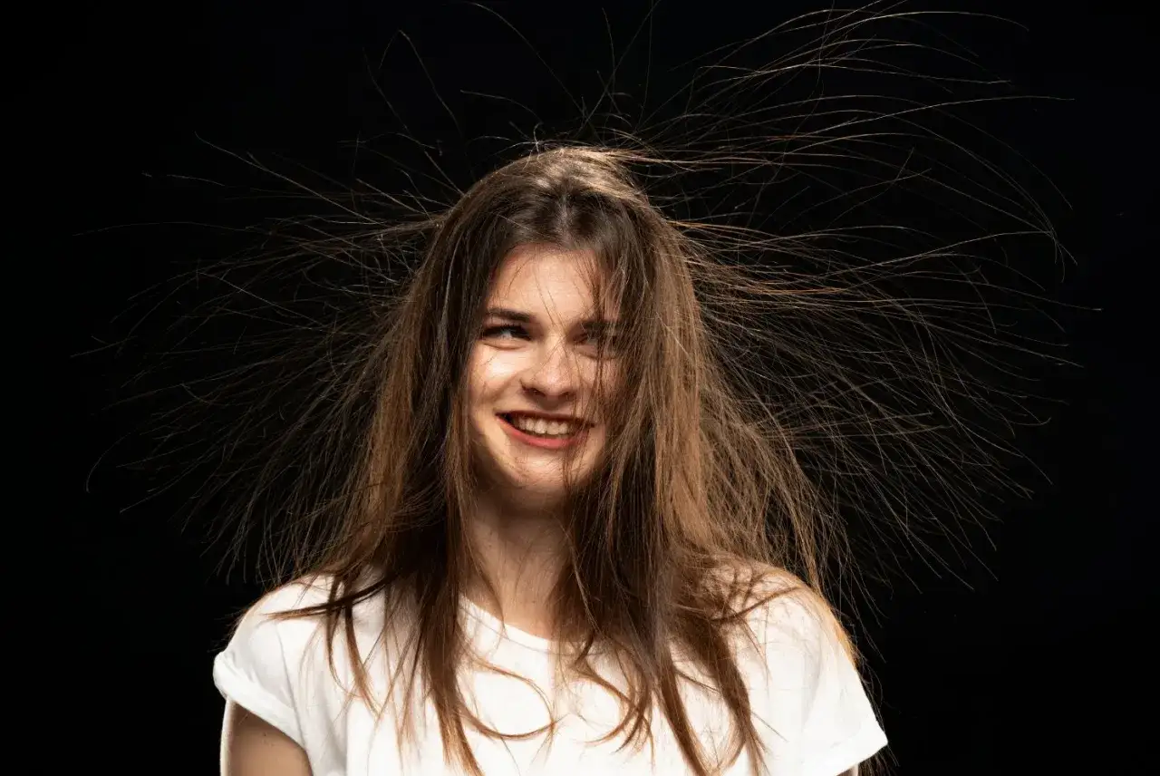 Ragazza con capelli elettrizzati che sembrano esplodere in tutte le direzioni, con un sorriso birichino.